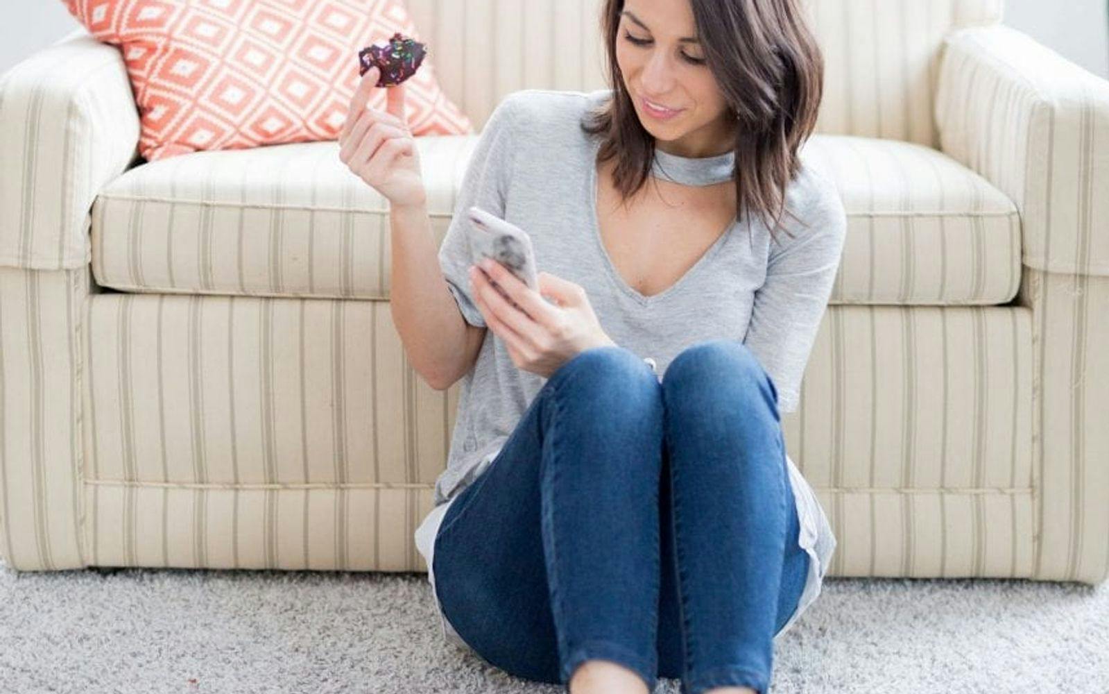 Kvinne foran en sofa med donut og iphone