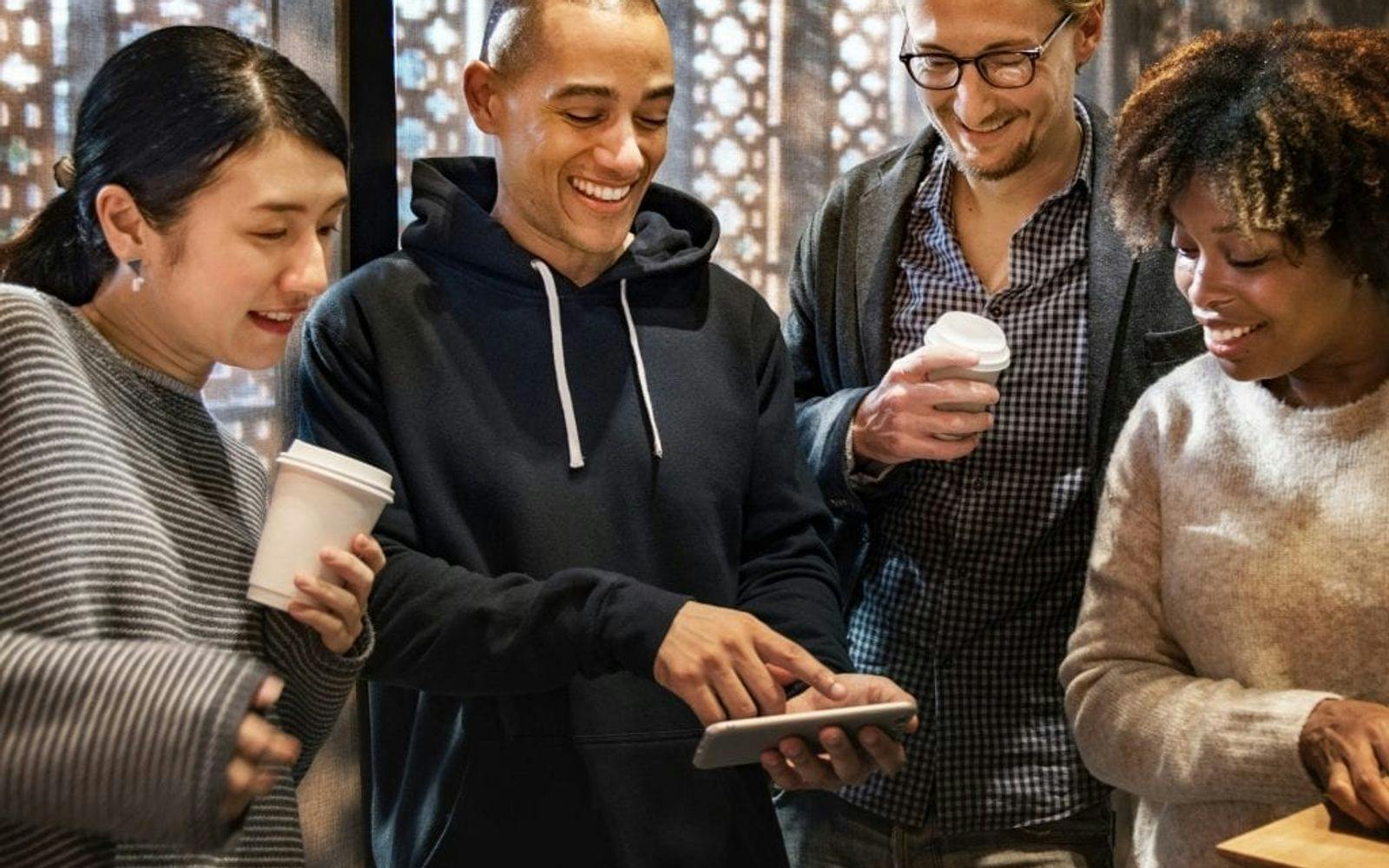 Gruppe smilende mennesker som ser på en smarttelefon